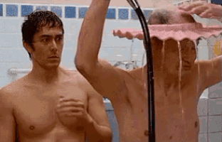 two shirtless men are taking a shower in a bathroom with a pink shower head .
