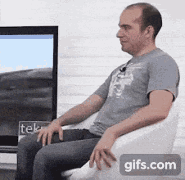 a man is sitting on a bean bag chair in front of a tv screen that says tek