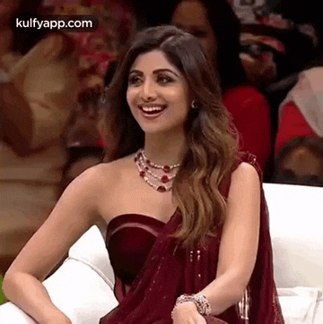 a woman is sitting on a couch wearing a red saree and a necklace .