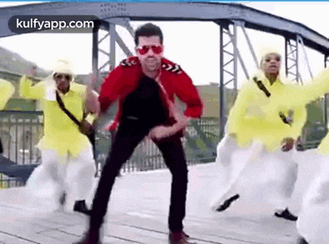 a man in a red jacket is dancing on a bridge with a group of people .