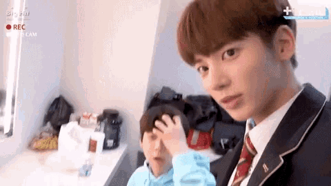 a boy in a suit and tie looks at the camera with a big hit logo on the bottom right