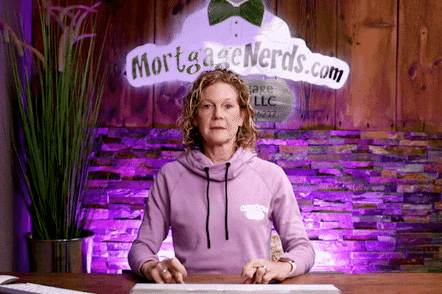 a woman sitting at a desk with a mortgage nerds.com sign behind her