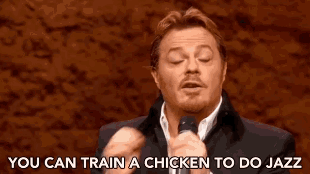 a man singing into a microphone with the words " you can train a chicken to do jazz " behind him