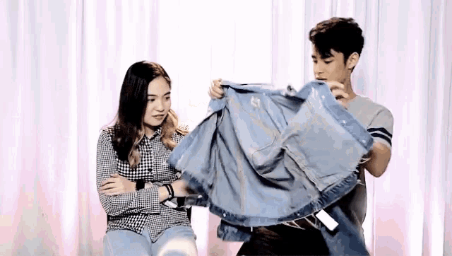 a man is holding a denim jacket while a woman looks on