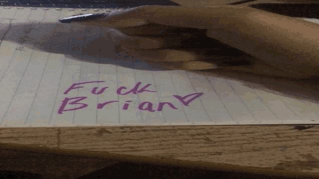 a person is writing in a notebook that says fuck brian
