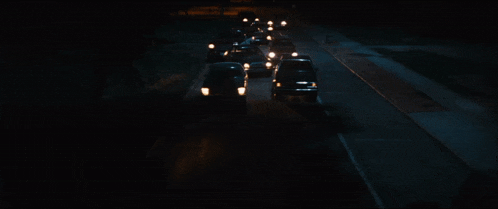 a row of cars are driving down a dark highway