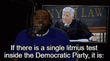 a man in a blue shirt is talking into a microphone in front of a judge