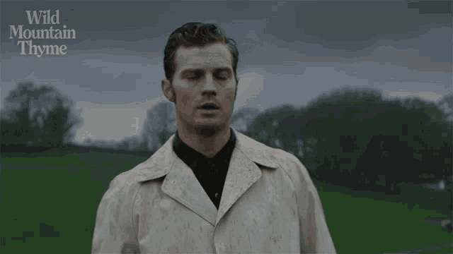 a man in a white coat stands in a field with the words wild mountain thyme above him