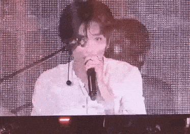 a man is singing into a microphone while sitting in front of a large screen .