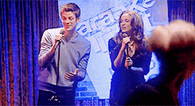a man and a woman are singing into microphones in front of a sign that says gfd