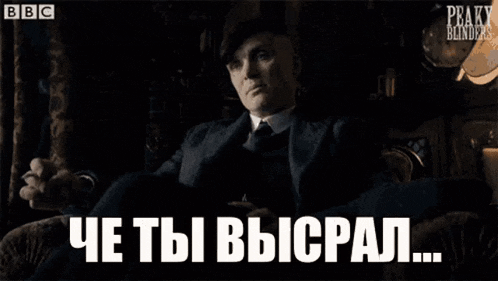a man in a suit and hat is sitting in front of a window with the words peaky blinders in white letters .