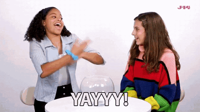 two girls are sitting at a table and one of them is saying yayy
