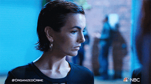 a woman is standing in front of a blue wall with the words organized crime on the bottom right