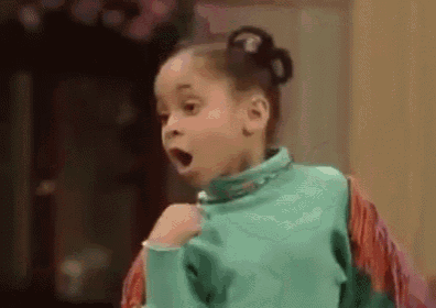 a little girl in a green sweater is making a surprised face with her mouth open .