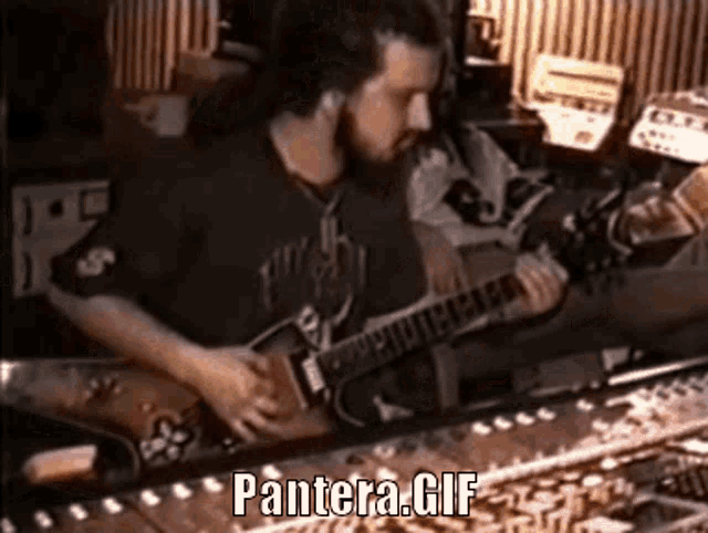 a man with a beard is playing a guitar in a room with the words pantera gif below him .