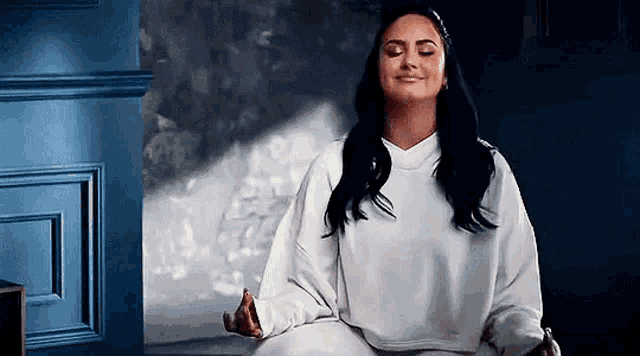 a woman is sitting in a lotus position with her eyes closed and her hands folded .