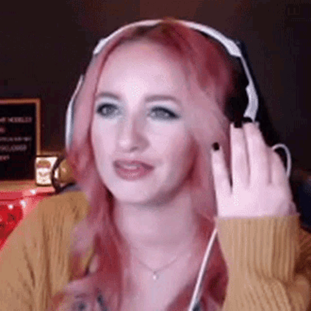 a woman with pink hair wearing headphones and a yellow sweater is making a funny face .