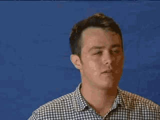 a man wearing a plaid shirt is smiling in front of a blue wall