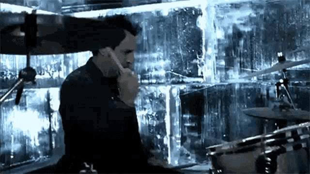 a man is playing a drum set in front of a wall of ice .