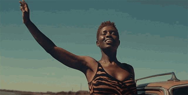 a woman in a zebra print tank top is standing next to a car