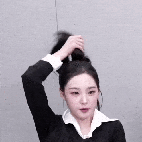a woman in a black sweater and white shirt is tying her hair in a ponytail .