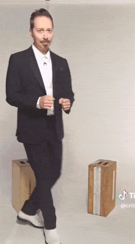 a man in a suit and white shoes is standing next to a box that says crate on it