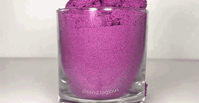 a glass filled with purple sand is sitting on a white table .