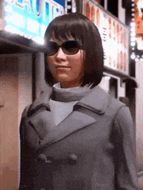 a woman wearing sunglasses and a coat is standing in front of a building with a sign on it .