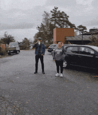a man and a woman are standing in a parking lot and the woman is wearing a sweater that says broken ny