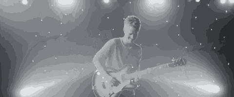 a black and white photo of a man playing a guitar on a stage .