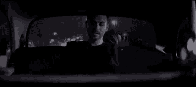 a man is sitting in the back seat of a car at night and looking out the window .