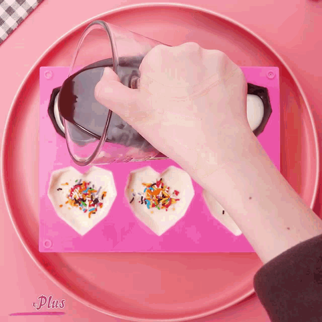 a person is pouring chocolate into a heart shaped mold with sprinkles