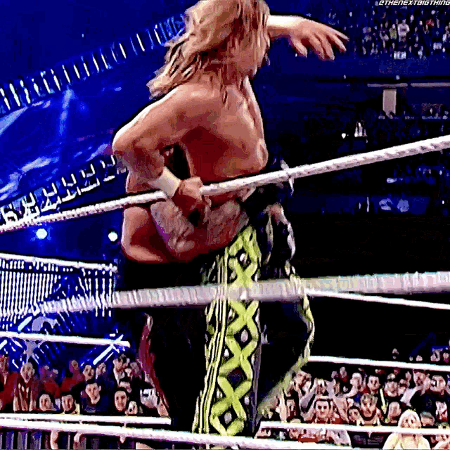 a wrestler is standing in a wrestling ring holding a rope .