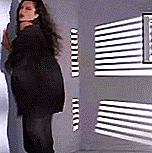 a woman in a black jacket is standing in front of a wall with striped blinds .