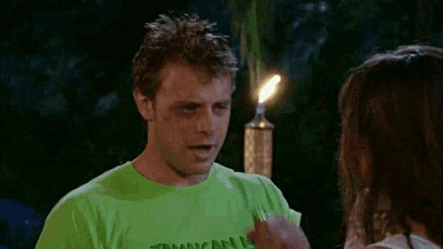 a man wearing a green t-shirt that says jamaican me drinks from a green bottle