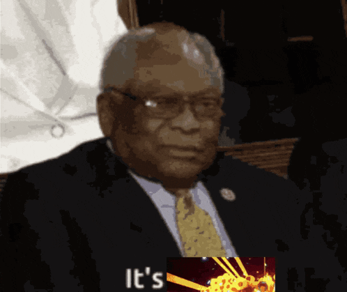 a man in a suit and tie is sitting in front of a picture that says ' it 's ' on it