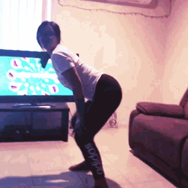 a woman wearing adidas leggings is squatting in front of a flat screen tv