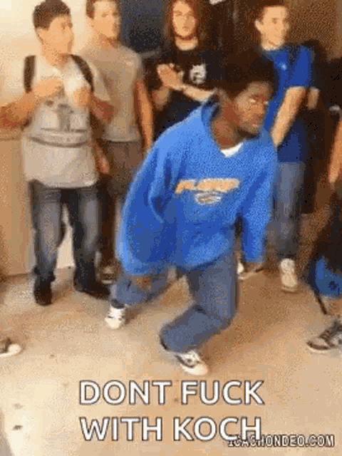 a man in a blue hoodie is dancing in front of a group of people and says `` dont fuck with koch '' .