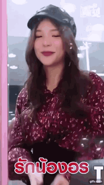 a woman wearing a hat and a leopard print shirt is smiling in front of a sign that says " t "