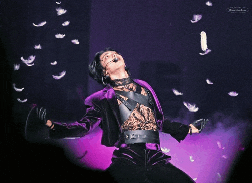 a man in a purple suit is surrounded by feathers and has a microphone on his head