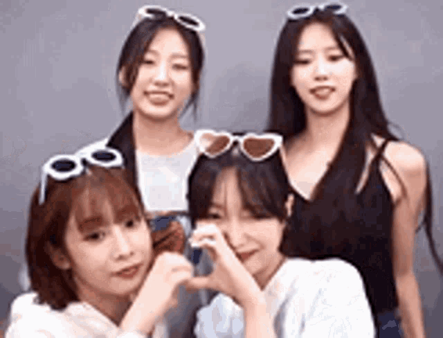 a group of young women wearing sunglasses are standing next to each other and making a heart shape with their hands .