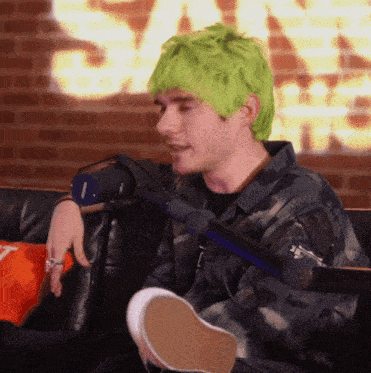 a man with green hair sits on a couch with a microphone