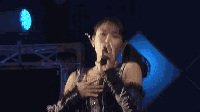 a woman is singing into a microphone with a blue light behind her