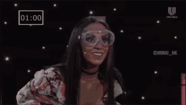a woman wearing goggles and a face shield is standing in front of a clock .