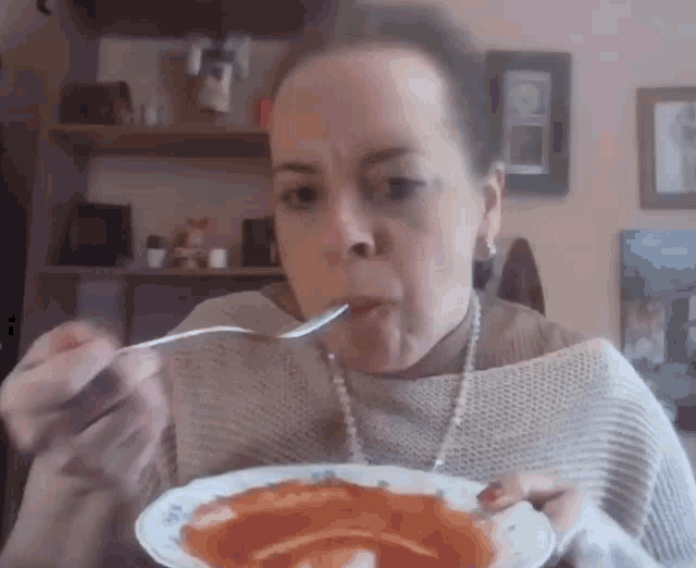 a woman is eating a plate of soup with a spoon in her mouth