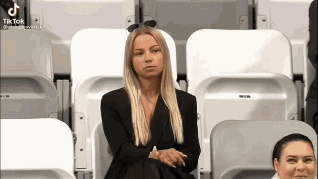 a woman is sitting in the stands of a stadium wearing sunglasses and a black jacket .