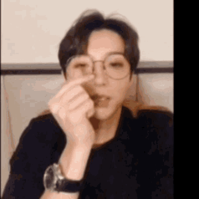 a man wearing glasses and a watch is making a heart shape with his finger .