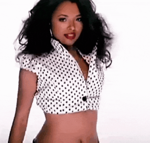 a woman is wearing a white polka dot crop top and earrings .
