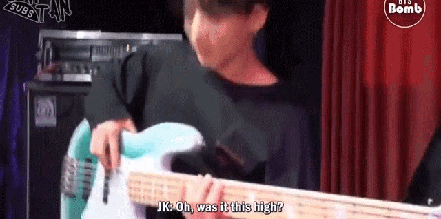 a man is playing a bass guitar on a stage and talking to another man .