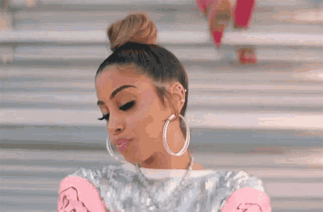 a woman wearing hoop earrings and a bun is standing in front of a set of stairs .